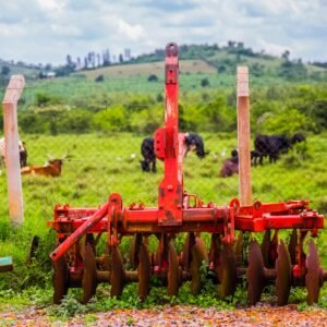 Vibrant red farm machinery against a green pasture with grazing animals, ideal for rural agriculture themes.